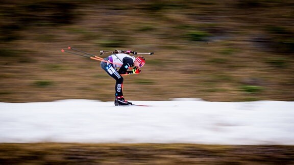Ein Biathlon-Athlet auf der Strecke, in einer schneefreien Umgebung.