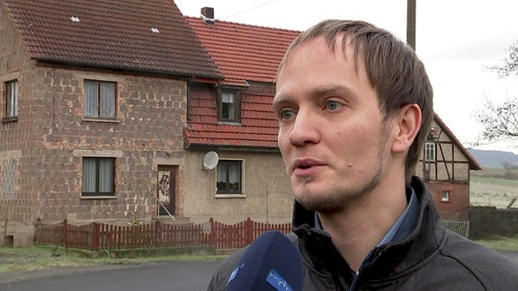 Ein Mann steht während eines Interviews vor einem Haus.