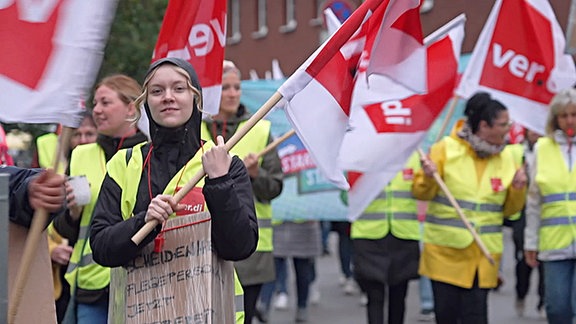 Bei einer Demonstration tragen Menschen gelbe Warnwesten und hlten Verdi-Fahnen in der Hand.