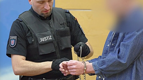Ein Justiz-Beamter nimmt dem Angeklagten die Handschellen ab.