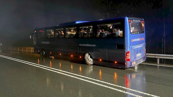 Ein blauer Reisebus mit gebrochenem Hinterrad im Dunkeln am Fahrbahnrand.