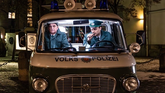 Ein Barkas-Auto, darin zwei Schauspieler in der Uniform von DDR-Volkspolizisten.