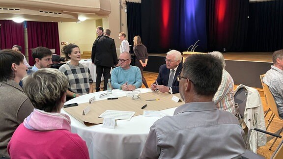 Bundespräsident Frank-Walter Steinmeier sitzt mit einer Gruppe Menschen an einem runden Tisch.