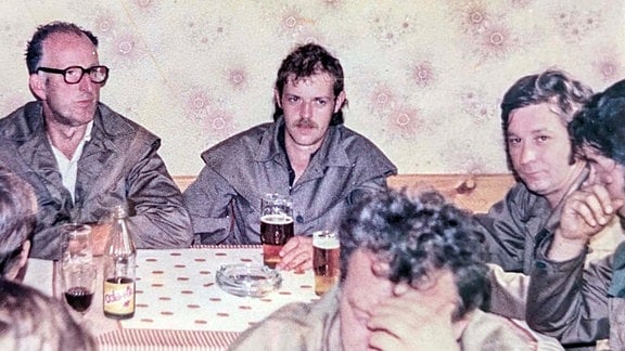 Altes Foto von Männern die in Mänteln an einem Tisch mit Aschenbecher sitzen und Bier trinken