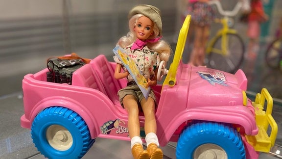 Eine Barbie-Puppe sitzt in einem rosa Wagen.