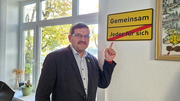 Uwe Scheler, Bürgermeister von Neuhaus am Rennweg zeigt auf ein Schild "Gemeinsam"