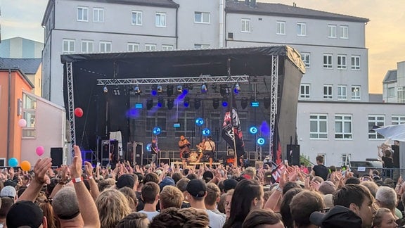 Mehrere hunderte Menschen stehen vor einer Bühne und jubeln der Band Feine Sahne Fischfilet zu. 