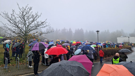 Menschen stehen im Nebel und Regen mit Schirmen vor dem Krankenhaus Neustadt.