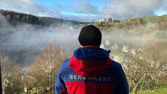 Ein Mann mit einer Bergwacht-Jacke schaut auf ein Tal