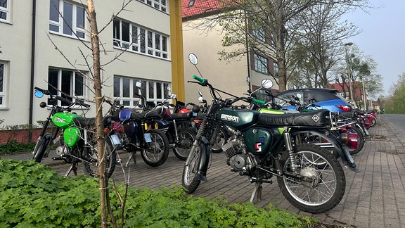 Zahlreiche Mopeds stehen vor einer Schule.