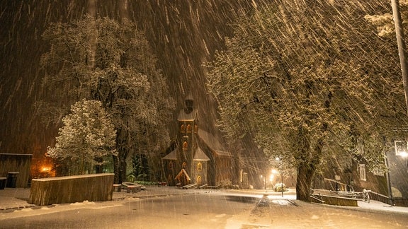 Starker Schneefall am Abend, im Hintergrund Bäume und eine Kirche.