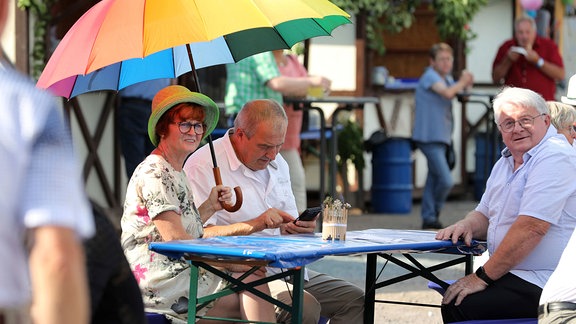 Drei Personen an einem Tisch mit einem bunten Regenschirm.