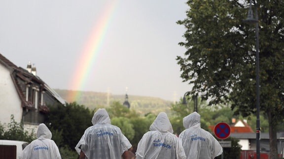 Menschen in Regenschutz, ein Regenbogen über dem Ort