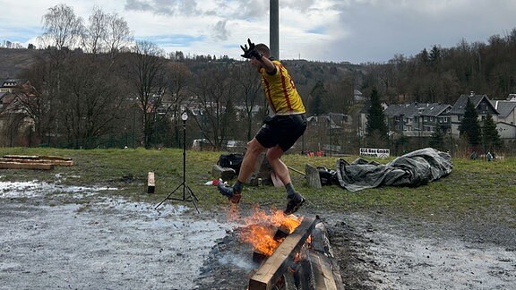 Mann springt über brennendes Holz 