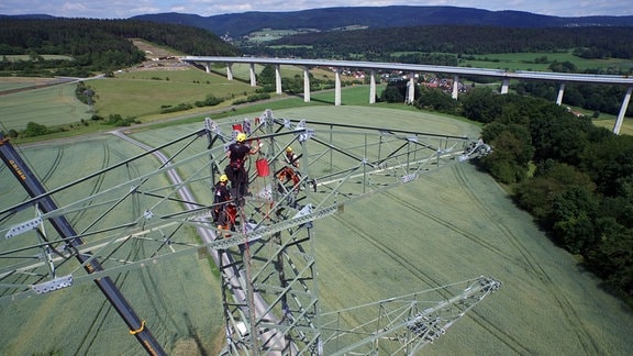 Monteure auf einem im Bau befindlichen Hochspannungsmast bei Schalkau im Landkreis Sonneberg. Im Hintergrund ist die ICE-Bogenbrücke Grümpental zu sehen. Die Baustelle ist Teil der Südwest-Kuppelleitung. Sie ist auch als Thüringer Strombrücke bekannt und eine 380-kV-Freileitung. 