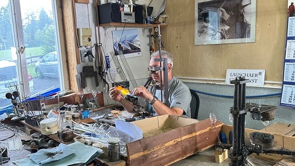 Ein Mann sitzt in seiner Werkstatt und bearbeitet Glas.