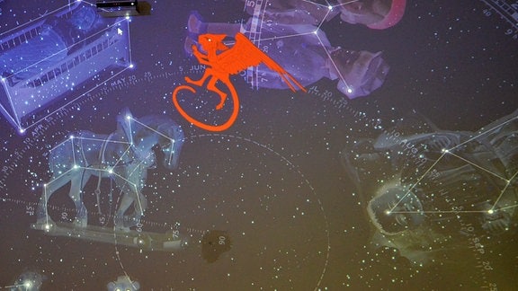 Projektion eines kleinen, roten Drachen mit Katzenkopf und Flügeln vor einer dunkelblauen Wand mit Sternbildern.