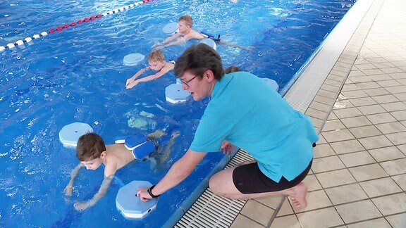 Eine Bademeisterin unterrichtet vom Beckenrand aus Kinder beim Schwimmkurs