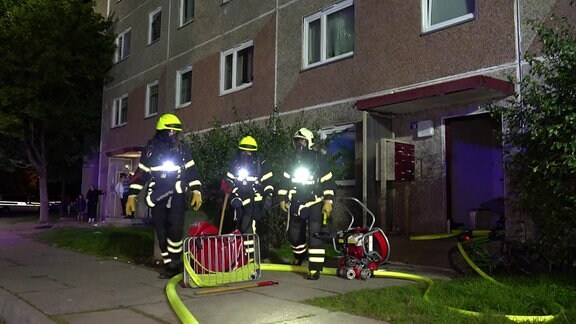 Drei Feuerwehrleute in Ausrüstung stehen vor einem Wohnahus.