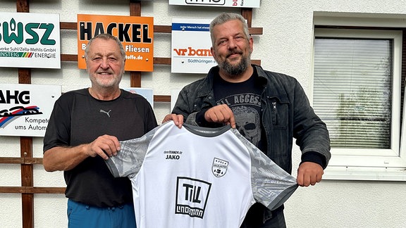 Zwei Männer halten ein weißes Trikot in den Händen.