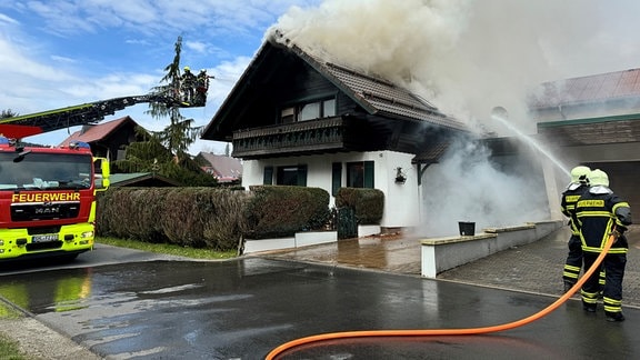 Feuerwehrleute löschen ein brennendes Wohnhaus.