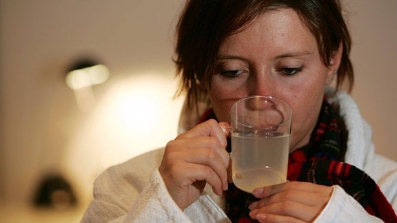 Erkältete Frau im Bademantel trinkt heiße Zitrone