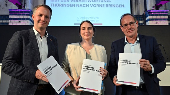 Andreas Bühl (l-r, CDU), Katharina Schenk (SPD) und Tilo Kummer (BSW) präsentieren eine Druckschrift mit den Ergebnissen der Sondierungsgespräche zwischen CDU, BSW und SPD in der Erfurter Zentralheize. 