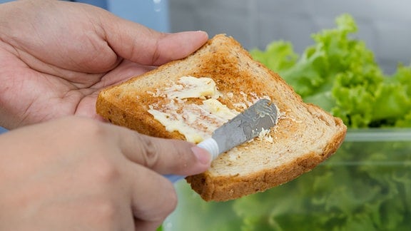 Eine Scheibe Toastbrot wird mit Butter geschiert.