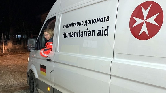 Eine Frau schaut auf der Fahrerseite eines Transporters aus dem Fenster.