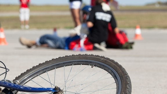 Fahrrad liegt am Boden, im Hintergrund wird ein Verletzter versorgt