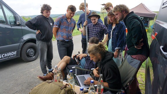 Eine Gruppe junger Menschen schaut auf einen Monitor an einem Feldrand