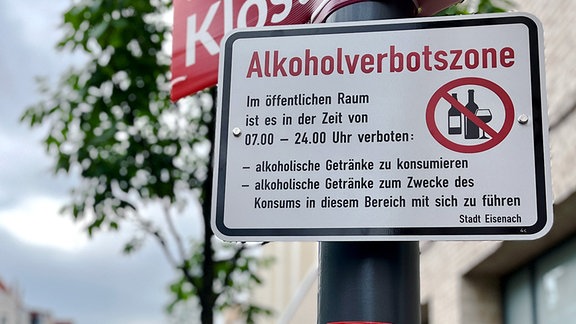 Ein Schild für eine Alkoholverbotszone hängt an einem Laternenpfeiler neben einer Straße.