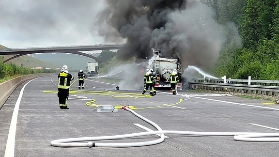 Mehrere Feuerwehrleute löschen einen brennenden Lkw-Anhänger auf einer Autobahn