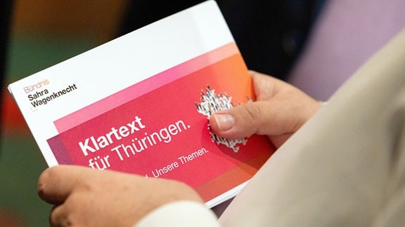 Ein Parteimitglied hält vor der Gründungsversammlung des Landesverbandes Thüringen Bündnis Sahra Wagenknecht (BSW) im Hotel «Thüringer Hof» eine Broschüre der Partei in der Hand.
