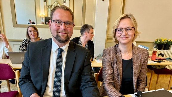 Christoph Ihling (CDU) und Katja Wolf (BSW, ehemals Linke) sitzen an einem Tisch im Rathaus. Auf dem Tisch steht ein Laptop und liegen verschiedene Unterlagen.