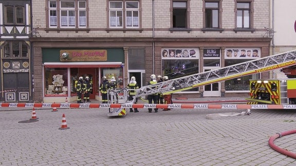 Feuerwehrleute stehen vor einem Haus. Hinter ihnen steht ein Leiterwagen.