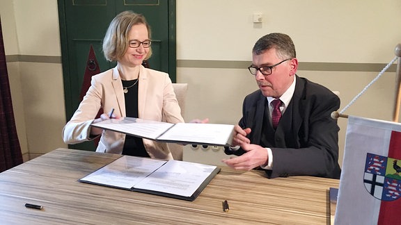 Katja Wolf, Oberbürgermeisterin von Eisenach, reicht ein Dokument an Reinhard Krebs, Landrat des Wartburgkreises, weiter.