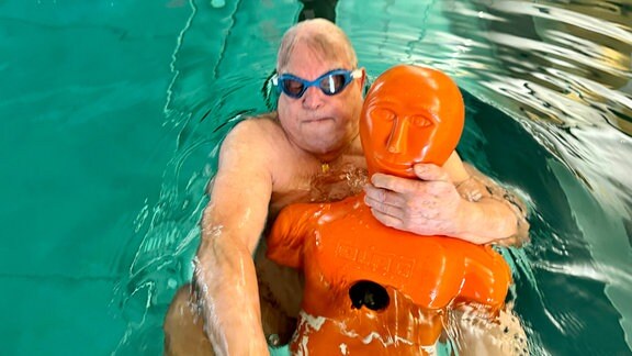 Ein Mann schwimmt während eines Rettungsschimmertrainings auf dem Rücken und hält eine Trainingspuppte im Arm.