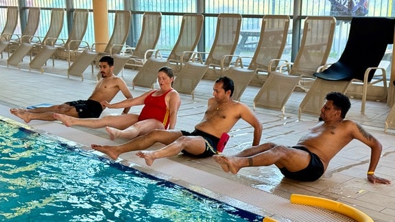 Drei Männer und eine Frau bei Schwimmübungen.