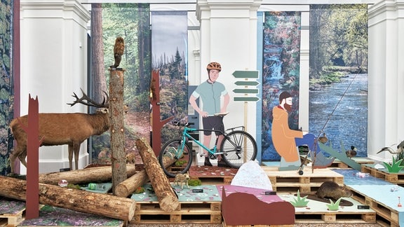 Ausstellung, Aufstellerfiguren von Menschen, ein ausgestopfter Hirsch, Holzstämme und andere Objekte.