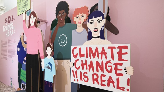 Aufstellerfiguren, die wie eine Demonstration wirken, ein Mädchen hält ein Schild mit der Aufschrift "Climate Change is real"