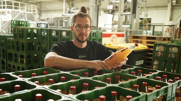 Florian Steinbrück, Chef der Fahner Frucht Handels- und Verarbeitungs GmbH aus Gierstädt, lehnt mit einer Flasche Apfelsaft in den Händen auf Getränkekästen.