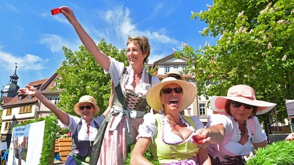 Vier Frauen in Trachten feiern ausgelassen und halten rote Schnapsfläschchen in die Luft