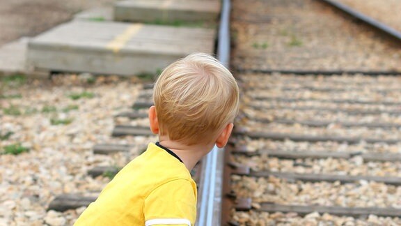 Junge schaut an Gleisen hockend nach einem Zug.