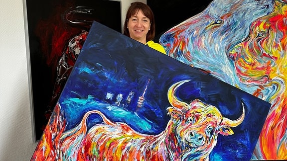 Künstlerin präsentiert buntes Stier-Gemälde vor blauem Hintergrund 