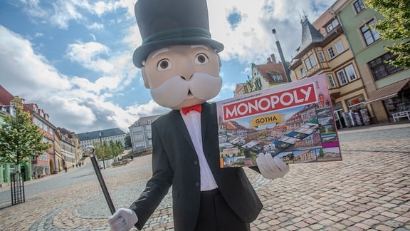 Ein als Mister Monopoly verkleideter Mensch hält in Gotha das neue Brettspiel in den Händen.