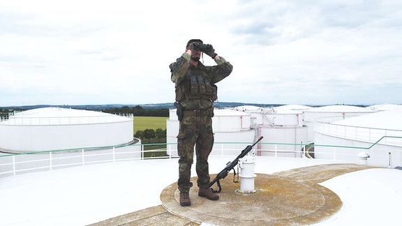Ein Soldat steht auf einem Silo und schaut durch sein Fernglas.