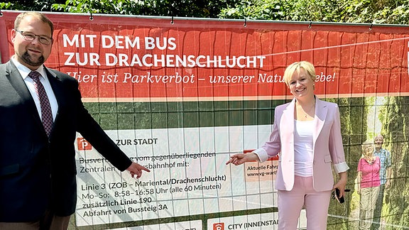 Zwei Personen stehen vor einem Banner mit dem Aufruf den Bus zu nutzen