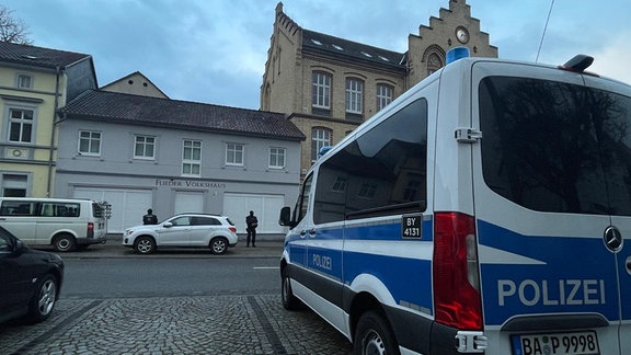 Polizisten und ein Polizeiauto vor einem Haus.