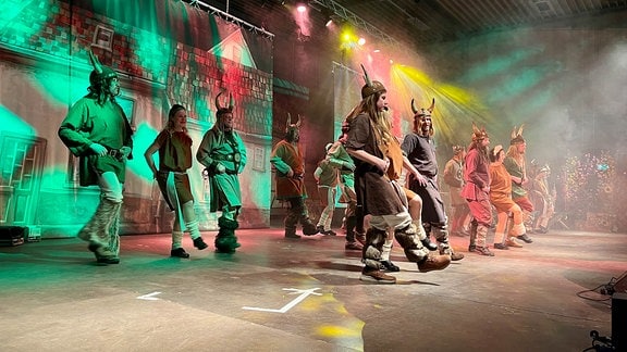Mehrere als Wikinger verkleidete Personen machen einen Line-Dance auf einer Bühne